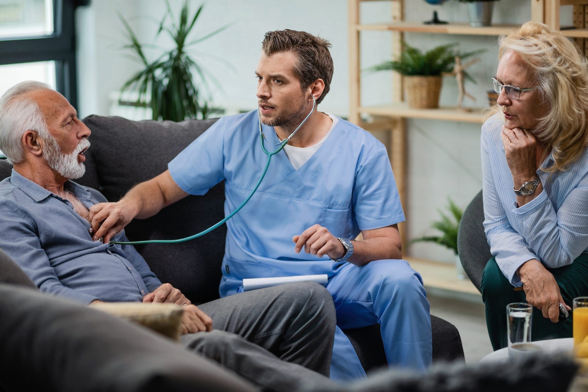 General practitioner examining senior man with a stethoscope and listening to his heartbeat during a home visit