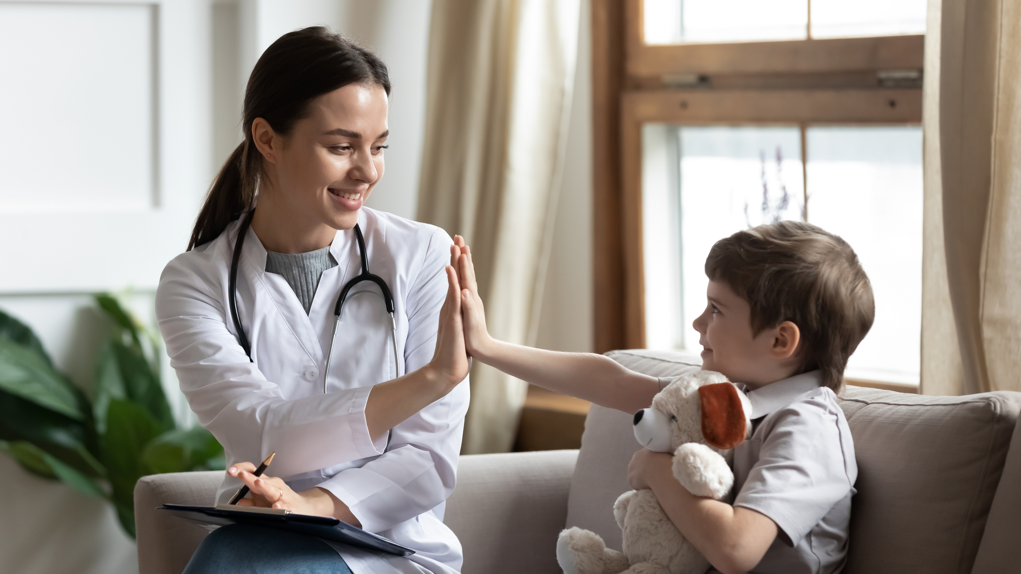 Smiling woman doctor or nurse give high five to excited little boy patient at consultation in clinic
