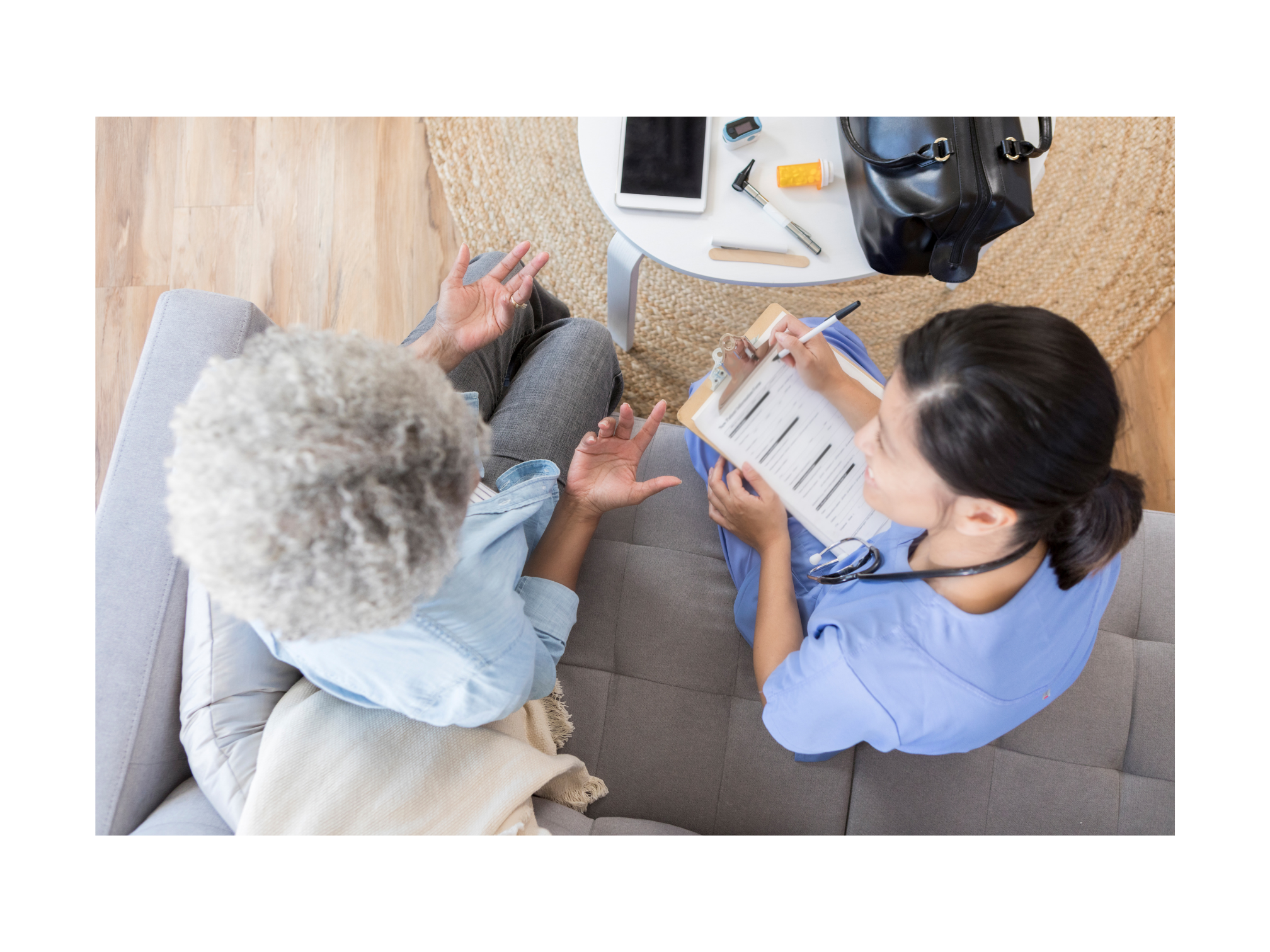 A healthcare professional in scrubs takes notes during a consultation with an older adult woman, emphasizing patient care and communication.